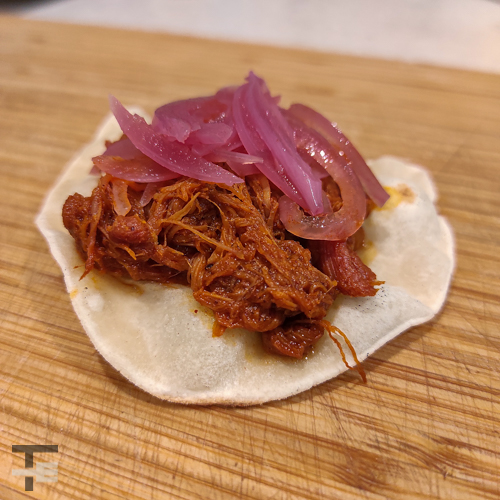 A mexican taco with cochinita pibil, a tortilla and pickled onion